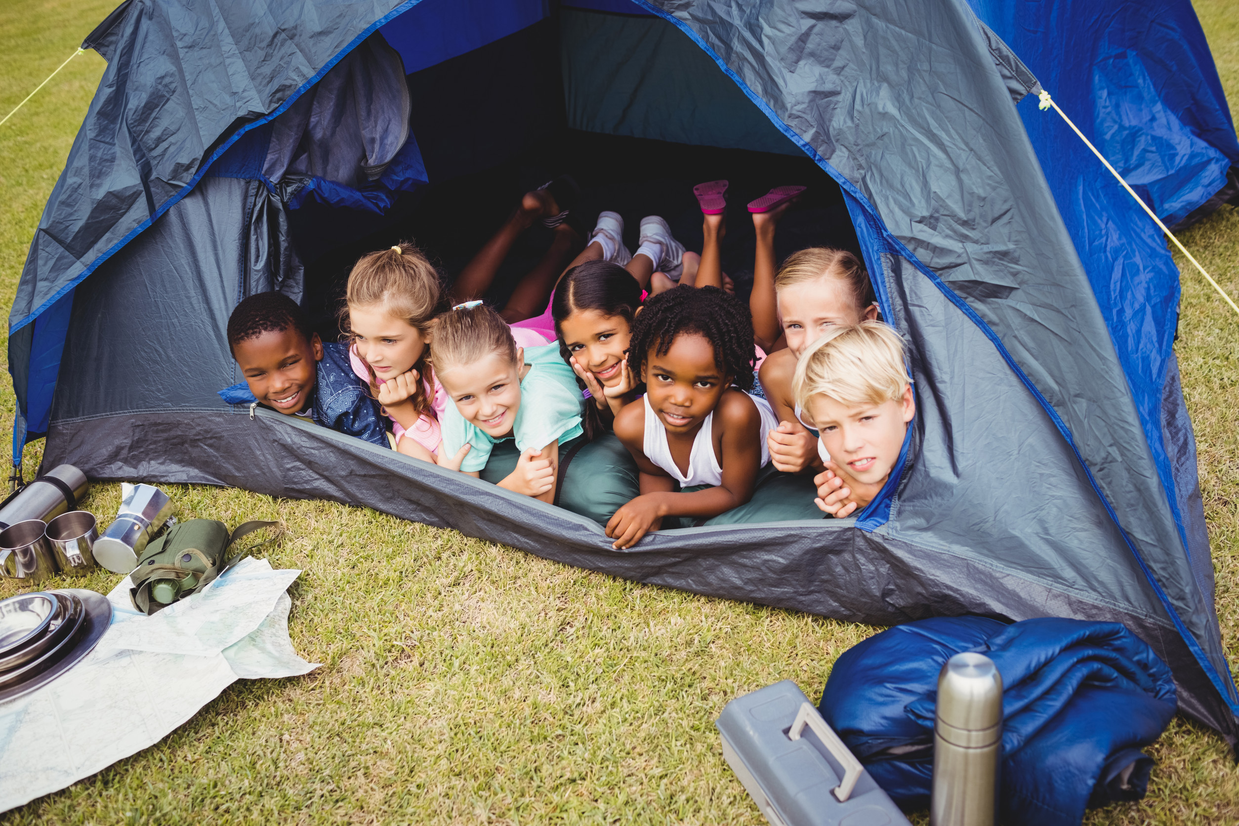 Smiling children lie down in the tent together in the park on a sunny day