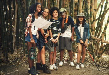 a group of teenagers looking at a map while exploring nature together at summer camp.