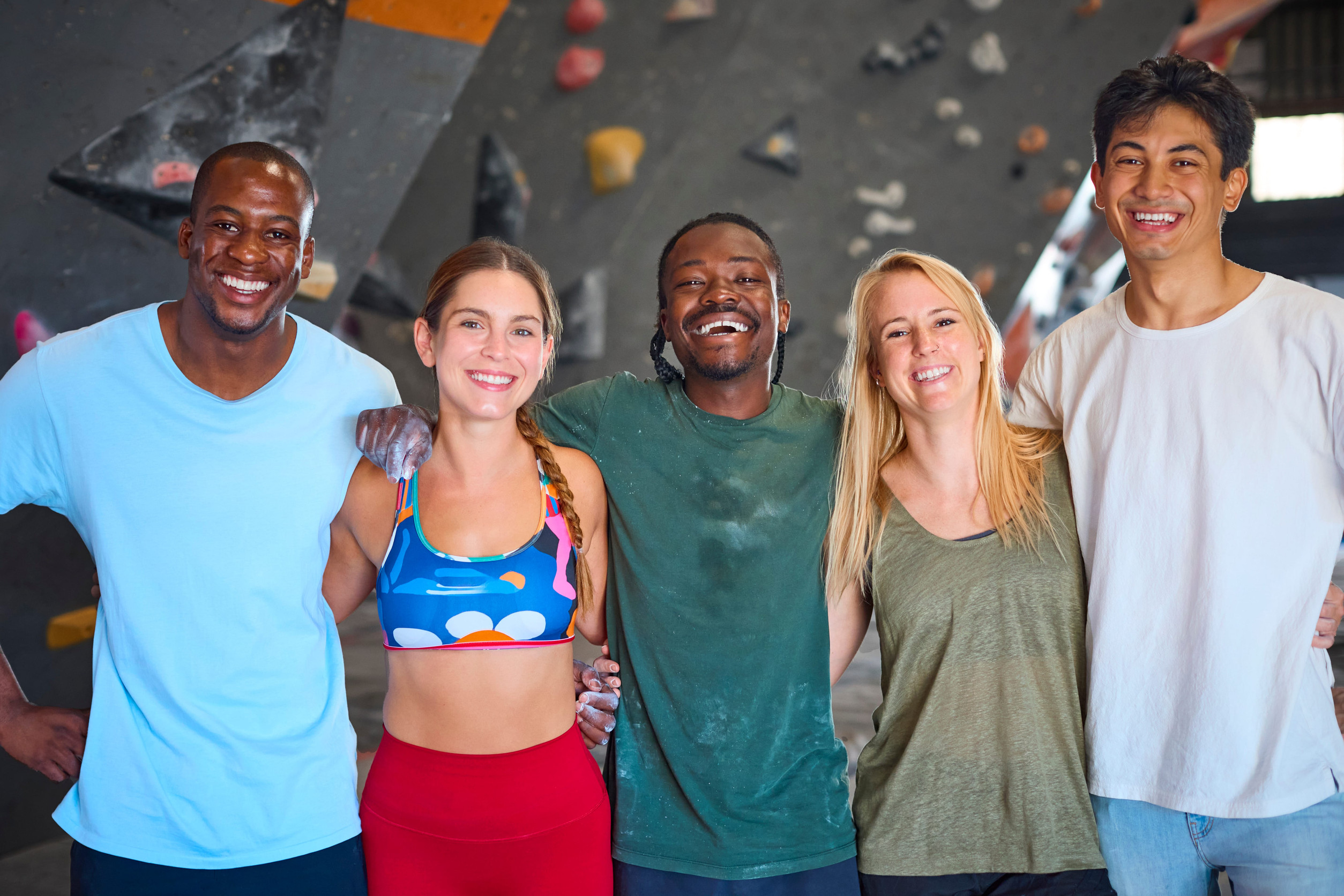 Portrait Of Climbers And Instructors Standing By Climbing Wall In Indoor Activity Centre